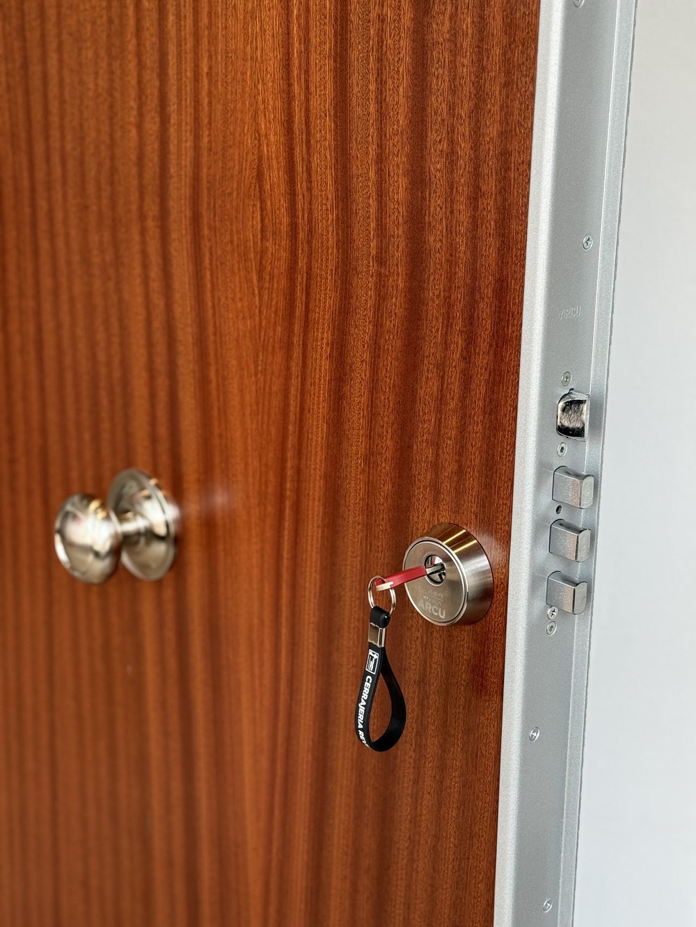 Puerta de madera entreabierta con llaves insertadas en la cerradura y un pasador metalizado visible.