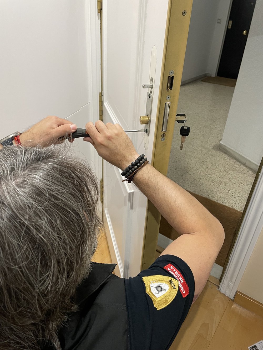 Persona arreglando una cerradura de puerta con destornillador, llaves insertadas, se ve uniforme y parche en el brazo.